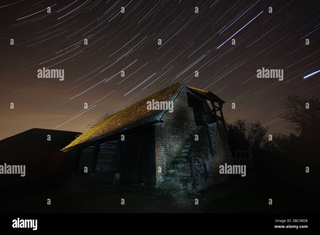Lunga esposizione di un fienile derelict in un paesaggio rurale con sentieri stellari nel cielo notturno. Foto Stock