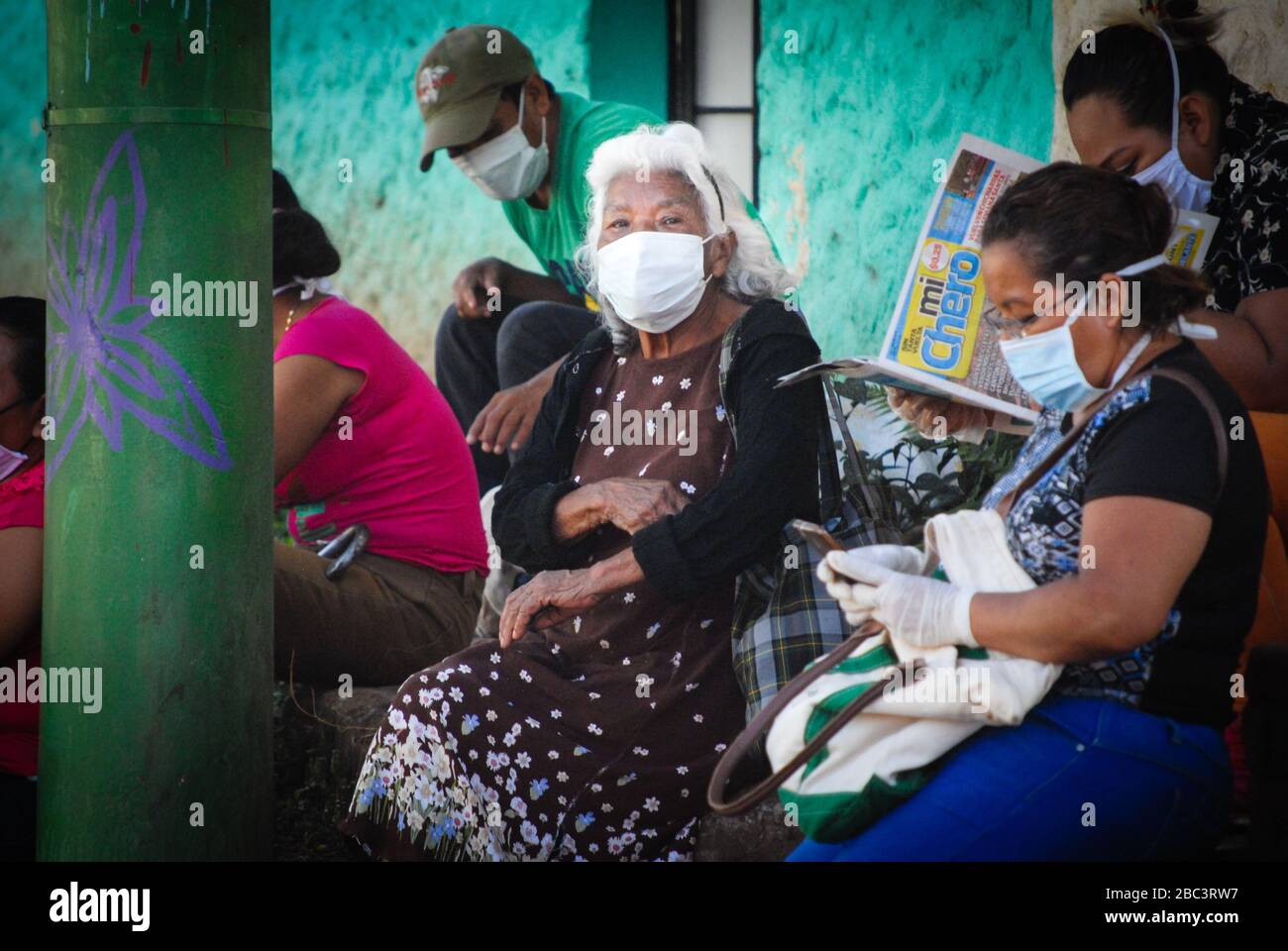 Persone che indossano maschere a Juayua, El Salvador in attesa per strada di ricevere aiuti pubblici per 300 dollari presso una banca locale. Foto Stock