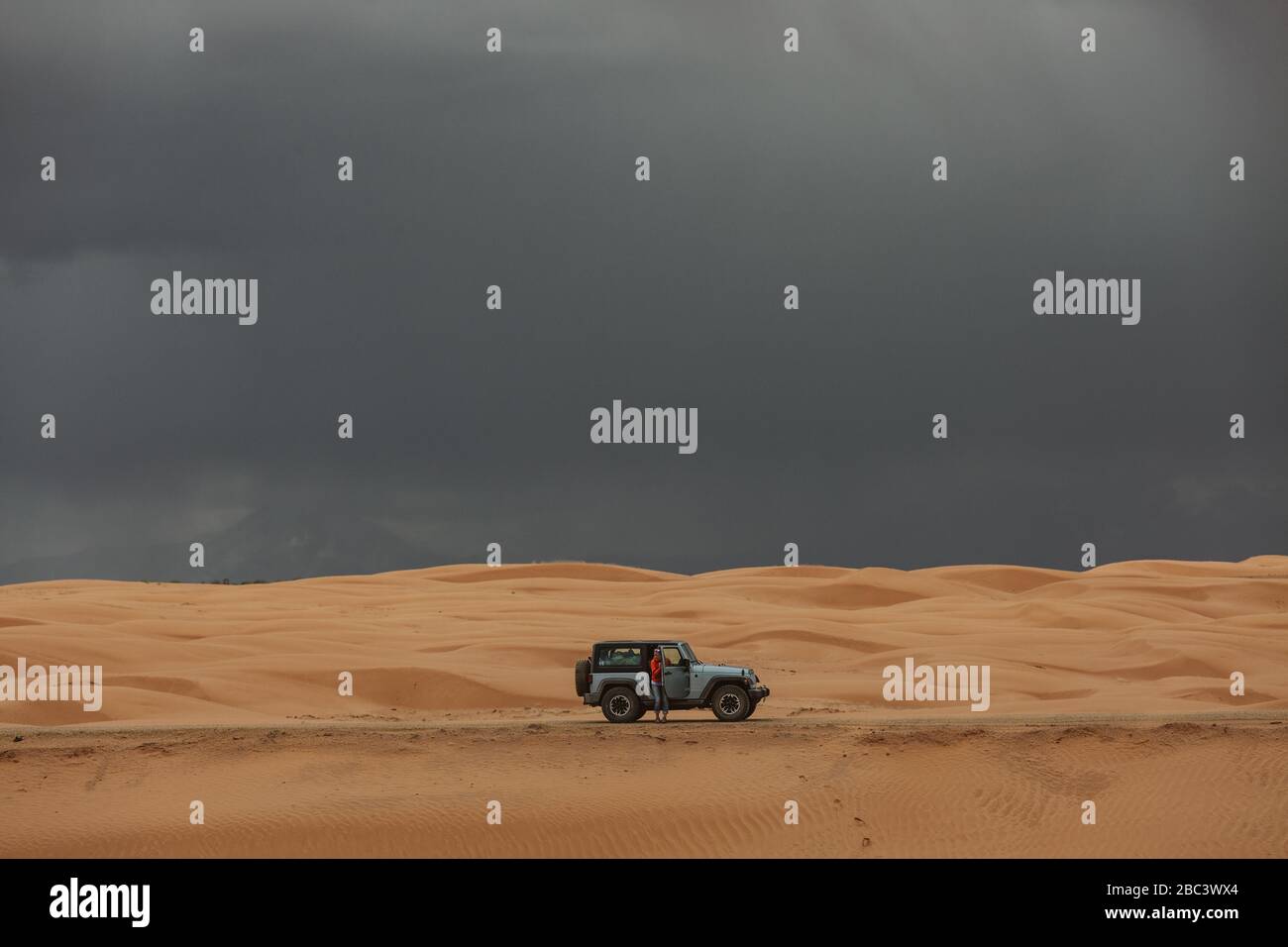 donna e la sua jeep mentre si guida attraverso dune di sabbia sotto il cielo tempestoso Foto Stock