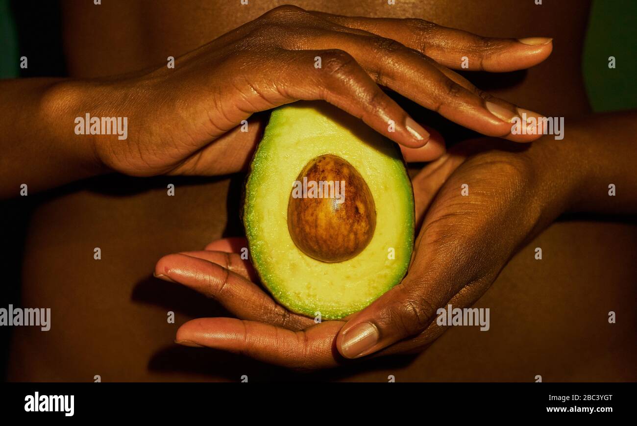 Mani scure in pelle che tengono un avocado. Concetto di Pregnacy Foto Stock