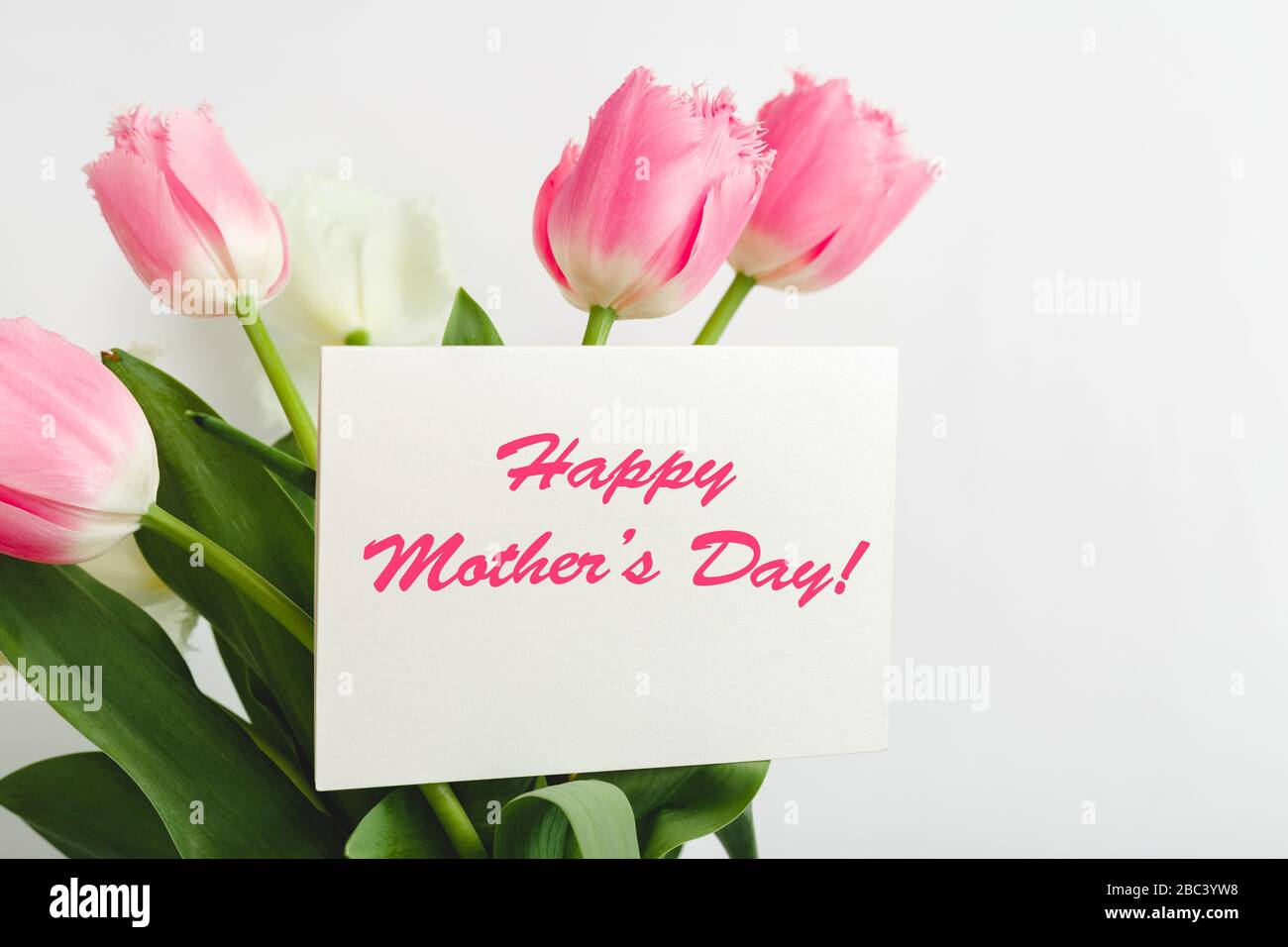 Testo Happy Mothers Day su carta regalo in bouquet di fiori su sfondo bianco. Biglietto d'auguri per mamma. Consegna fiori, carta Congratulazioni in fiori per Foto Stock