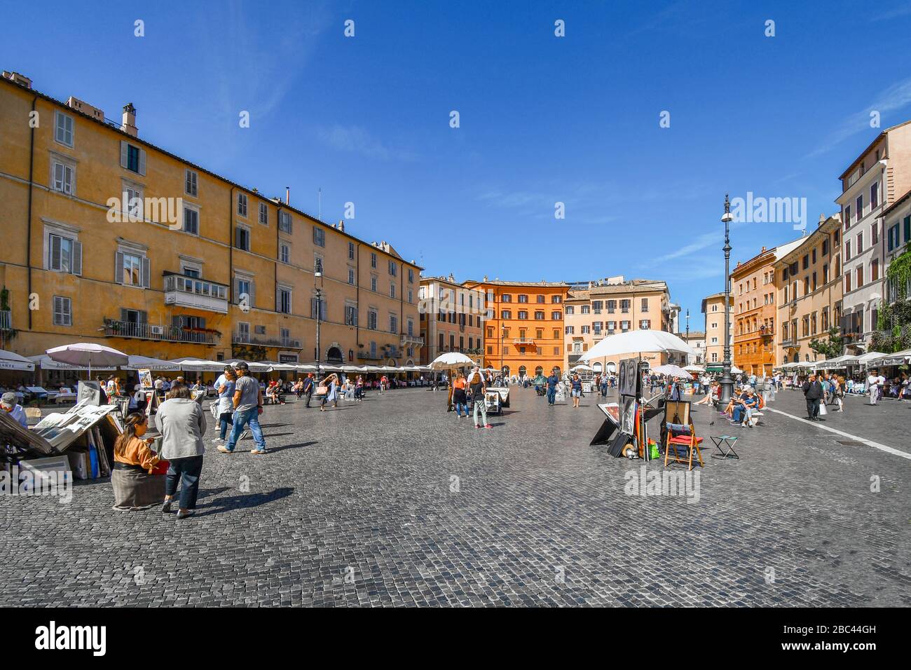 Una giornata di sole con un cielo blu nell'antica Piazza Navona mentre i turisti visitano e girovagano davanti ad artisti di strada che vendono le loro opere d'arte e dipinti. Foto Stock