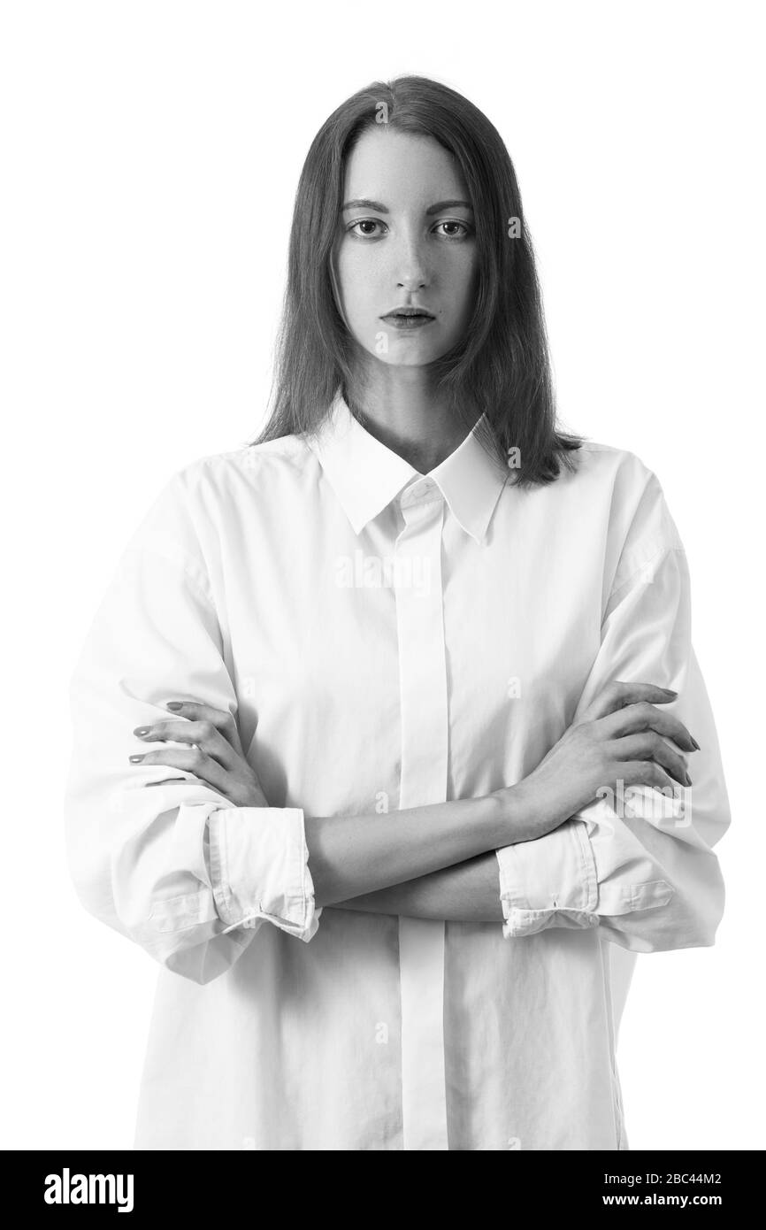donna giovane seria con le braccia incrociate in blusa bianca guarda la vista frontale della telecamera su sfondo bianco, monocromatica Foto Stock