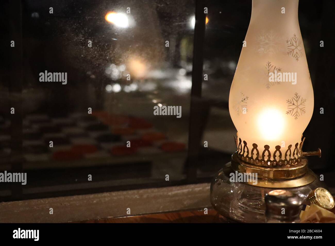 lampada hurricane con vetro smerigliato inciso con fiocchi di neve riflessi nella finestra di vetro Foto Stock