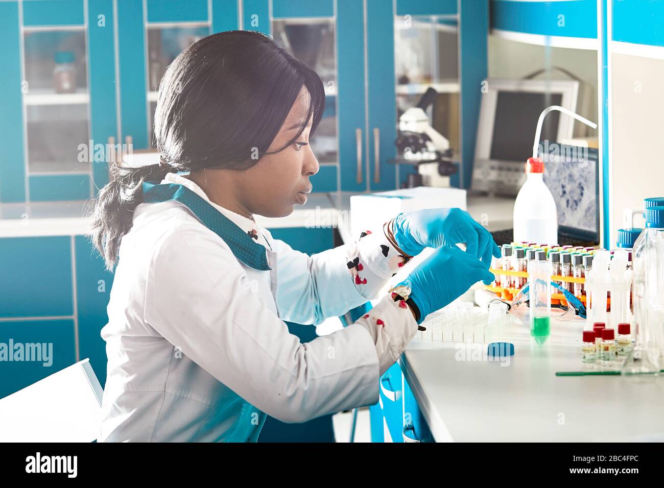 Lo scienziato africano o lo studente laureato in camice da laboratorio e guanti di nitril esegue test PCR di campioni di pazienti in un moderno laboratorio di test. Foto Stock