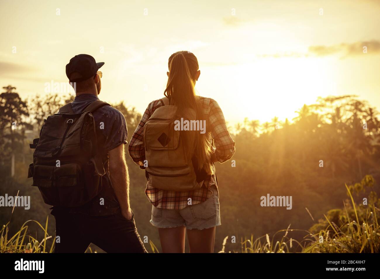 Un paio di viaggiatori si alza con zaini e guarda l'alba in tropici Foto Stock