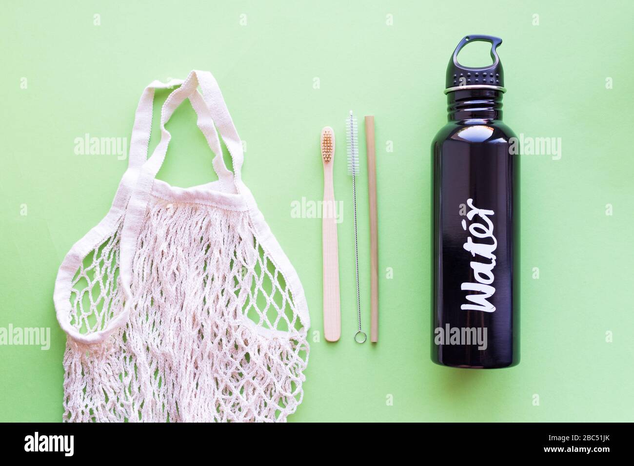 Concetto di zero sprechi. Cannuccia e spazzolino da denti in bambù, borsa in cotone e bottiglia d'acqua in metallo su sfondo verde. Vita sostenibile. Ecologico senza plastica Foto Stock