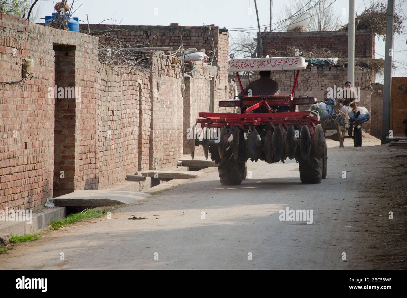 Un agricoltore guida attraverso una strada del villaggio con il suo tagliadischi meccanizzato nel distretto Sharaqpur della provincia di Punjab. Foto Stock