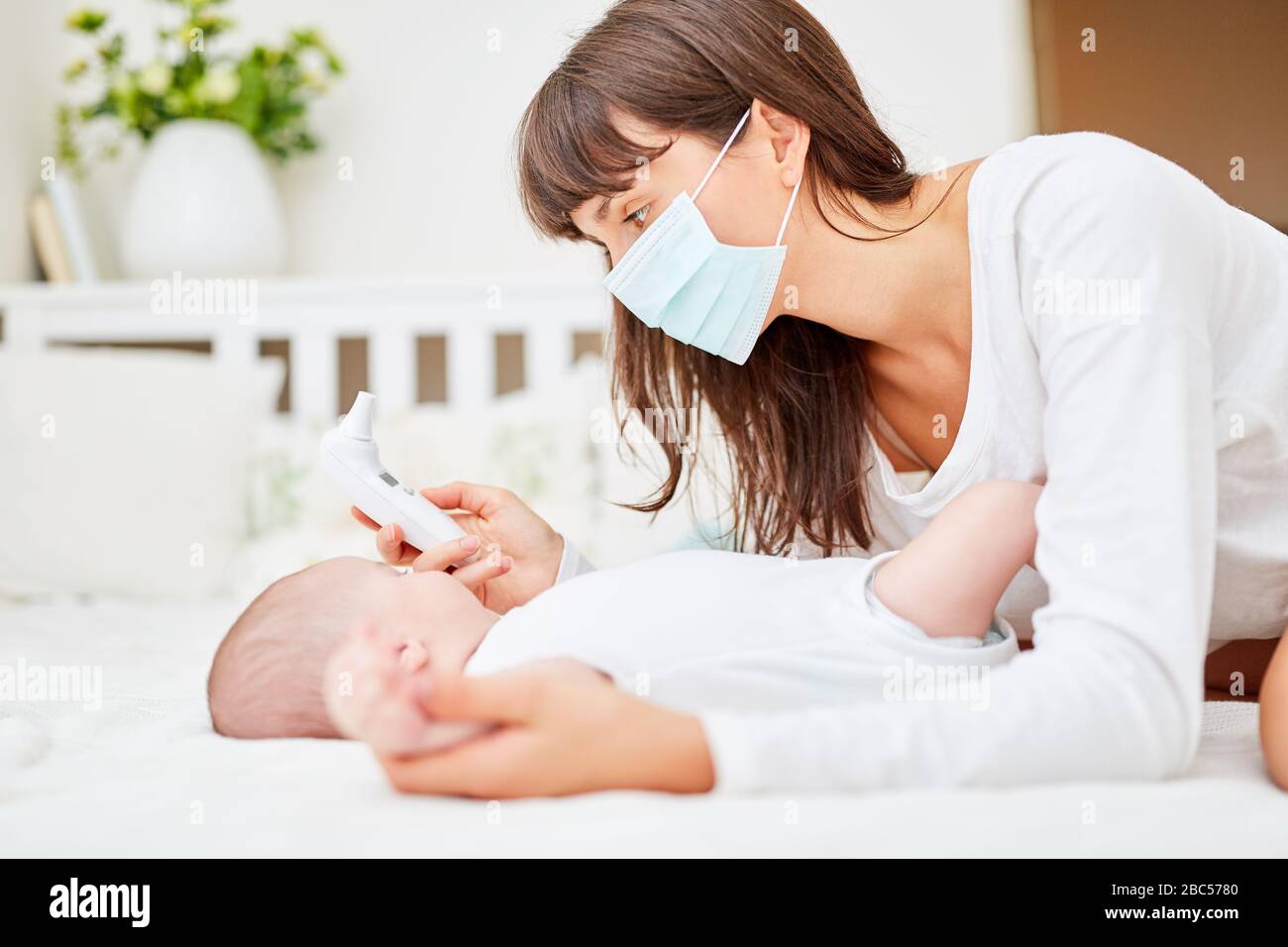 Madre con maschera facciale e bambino con misura di febbre con termometro auricolare Foto Stock