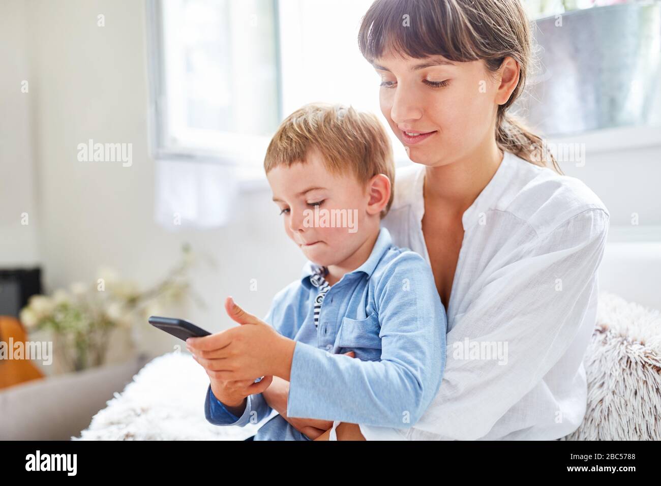 Il bambino gioca con lo smartphone in grembo a casa Foto Stock
