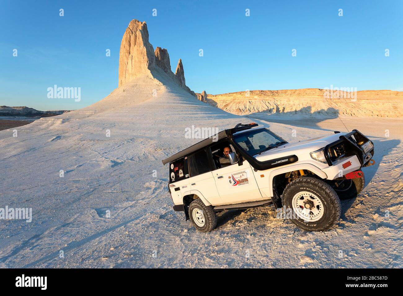 Sorridente pilota in Toyota Landcruiser alla guida di formazioni rocciose sceniche, Ustyurt Plateau a Boszhira, depressione Caspia, Aktau, Mangystau, Kazakhstan Foto Stock