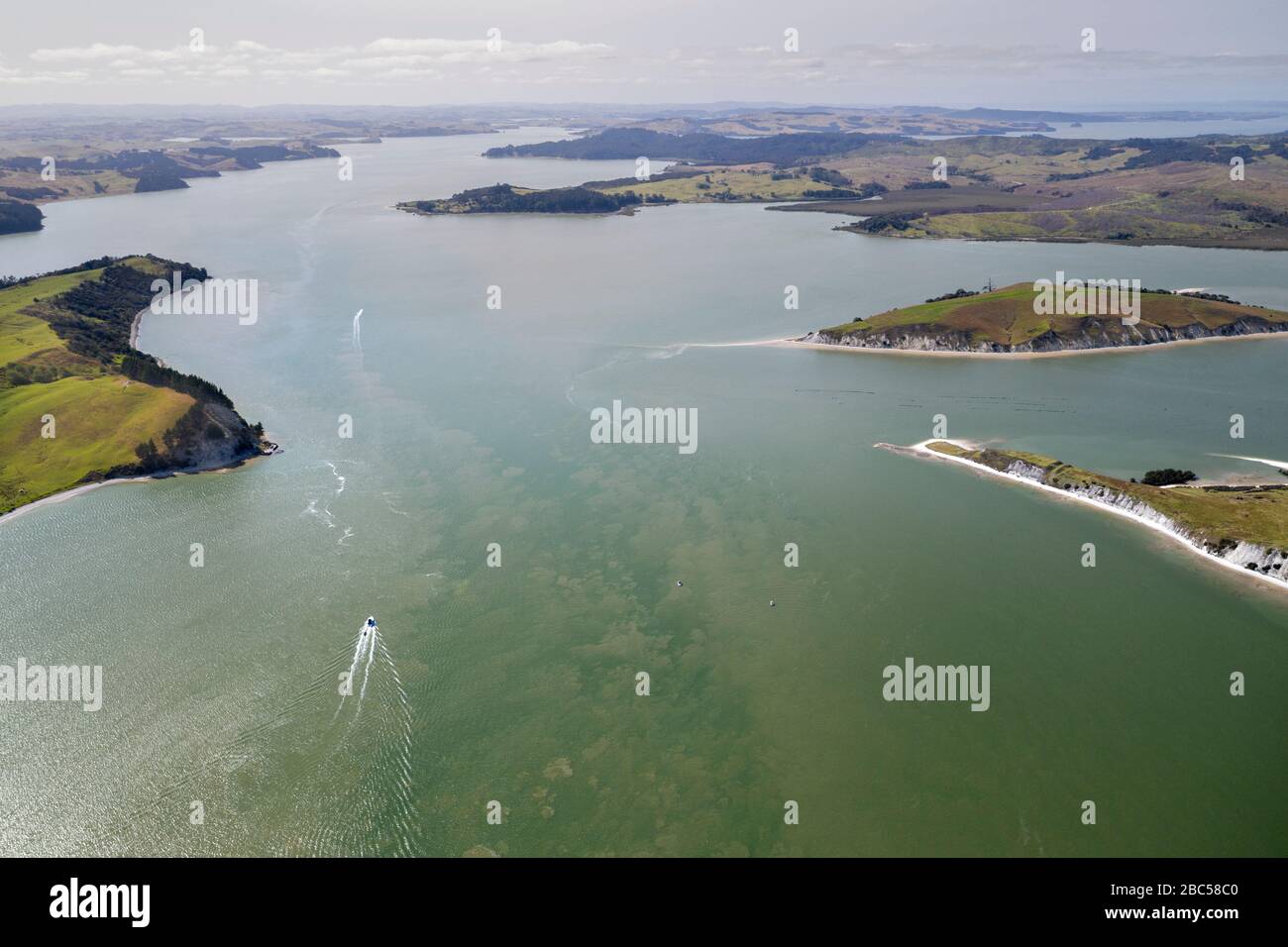 Vista aerea sul porto di Kaipara con un motoscafo sulle acque cristalline a Northland, Nuova Zelanda. Il paesaggio mostra alcune coste che si estendono fino alla fine di A. Foto Stock