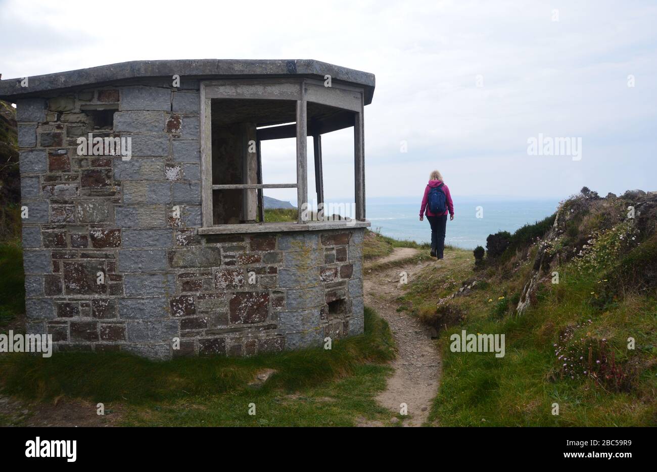 Lone Woman Hiker Walking by Disused Lookout Post on Higher Sharpnose Point on the South West Coastal Path, North Cornwall, England, UK Foto Stock
