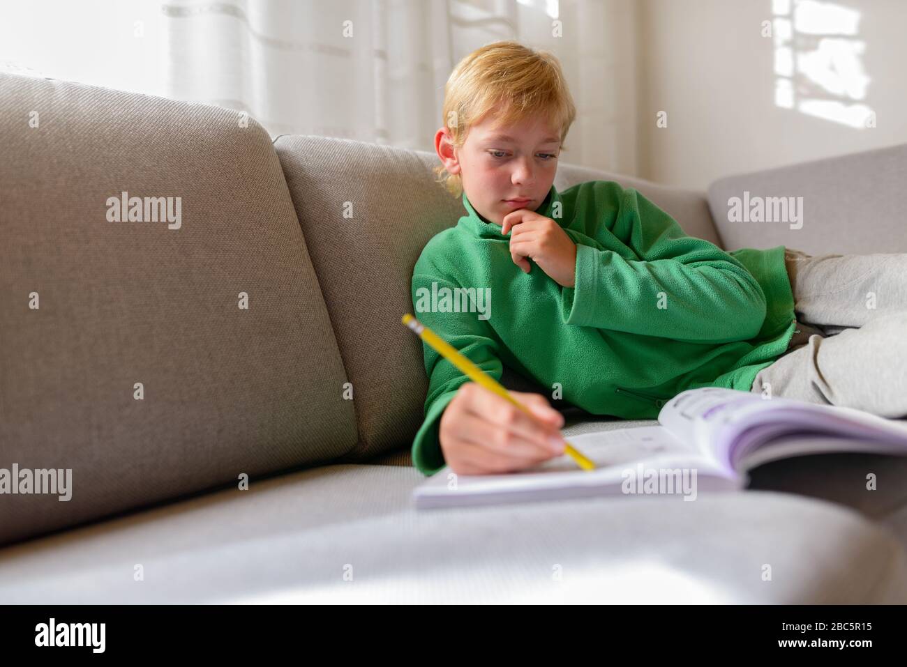 Giovane bel ragazzo che pensa mentre studia sul divano a casa Foto Stock