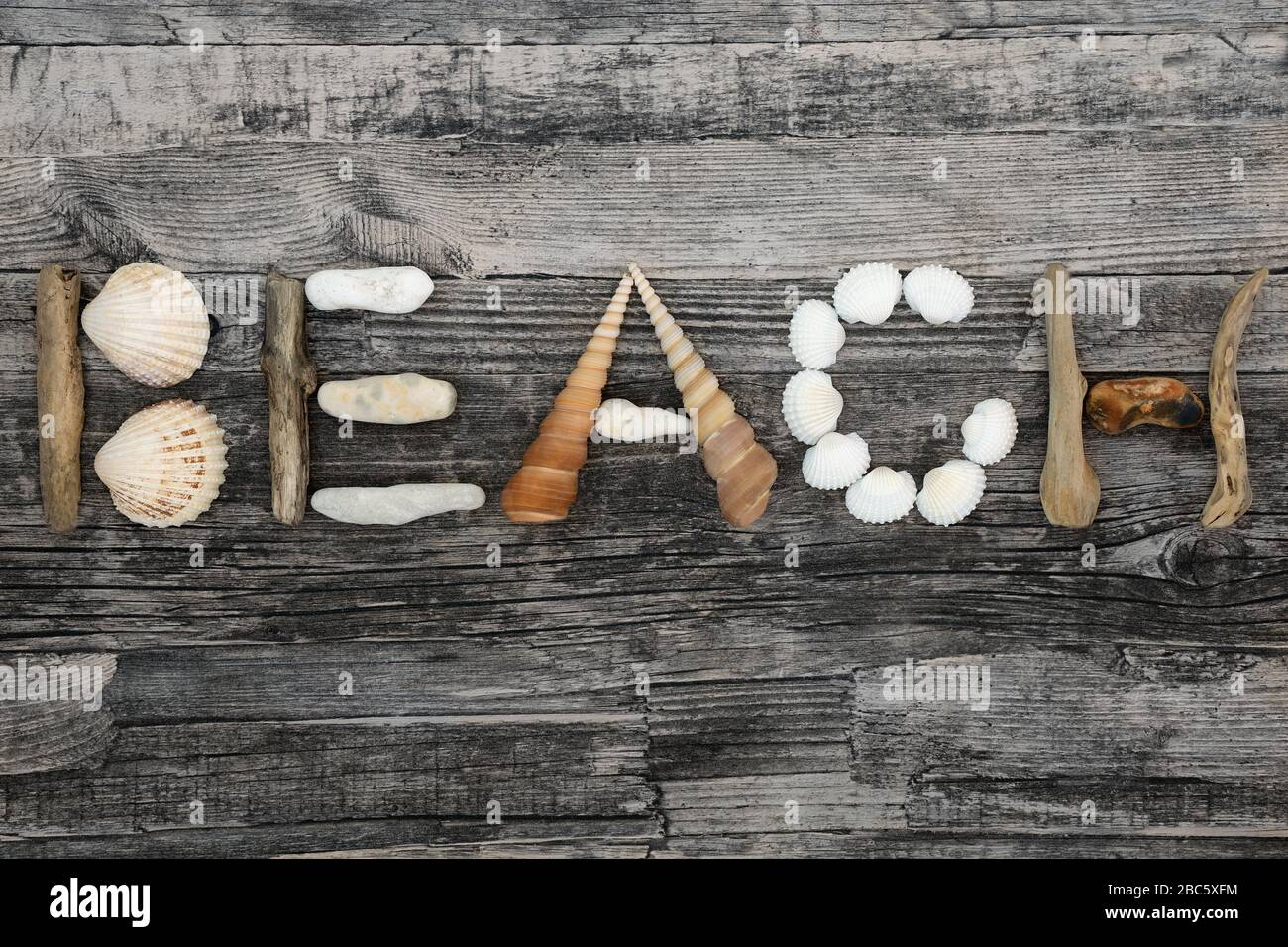 Astratto di conchiglie, driftwood e ciottoli che formano la parola spiaggia su sfondo rustico legno. Sfondo del concetto di vacanza. Foto Stock