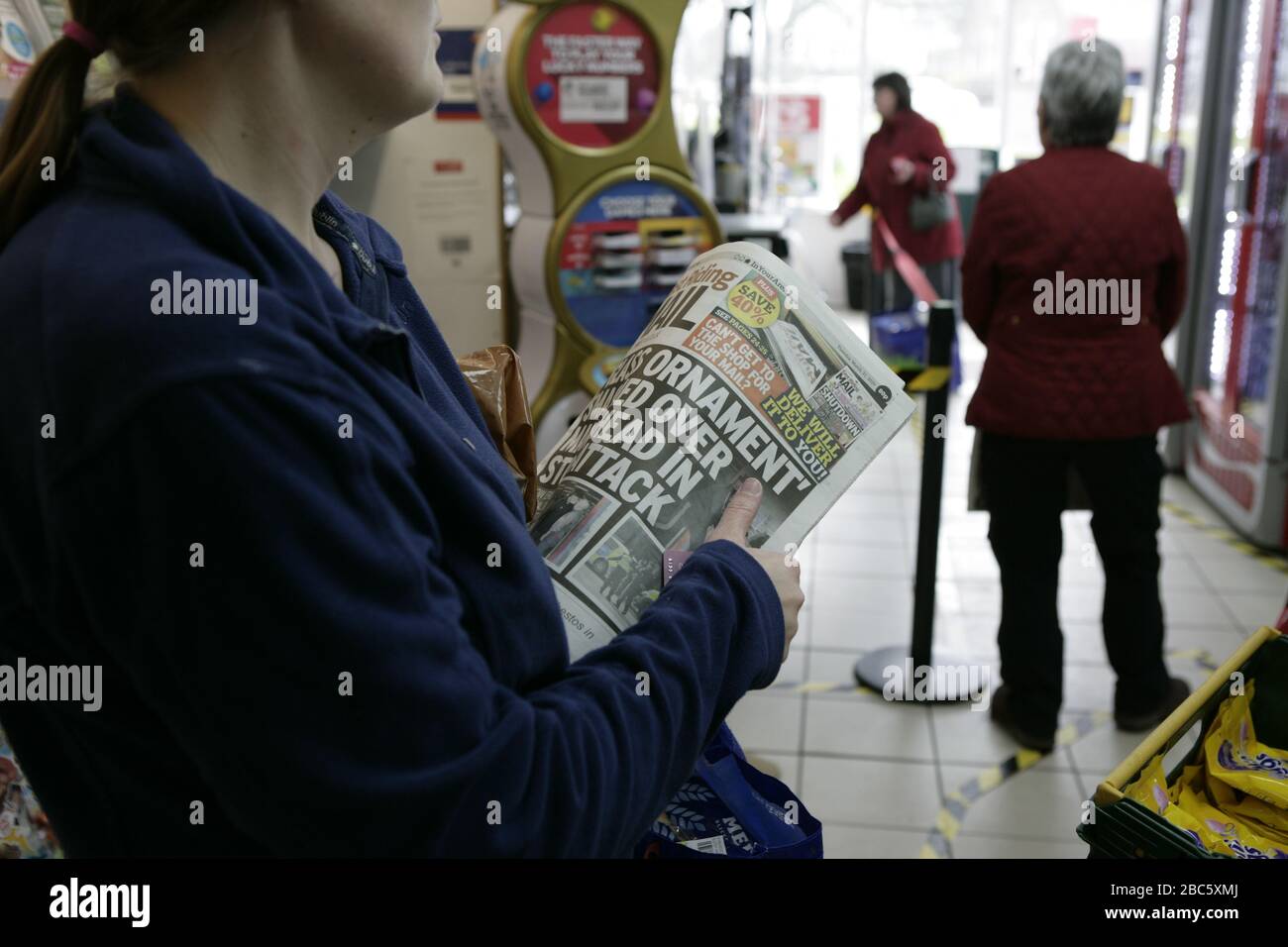La donna si è levata in piedi nella coda di allontanamento sociale che legge le notizie principali della pagina anteriore che attendono per comprare il giornale orientale della posta di Riding durante la pandemia di coronavirus Foto Stock