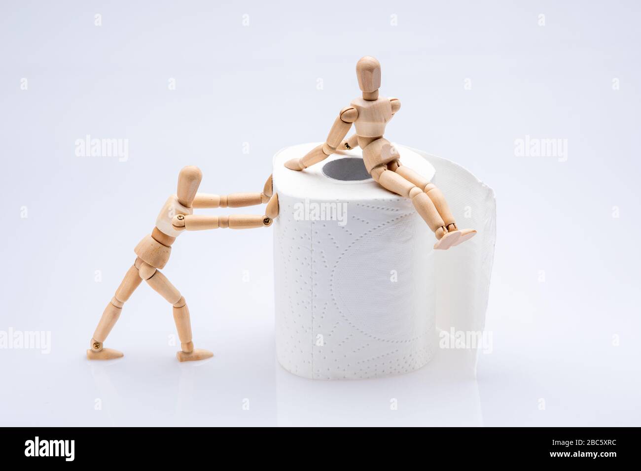 Persone di legno che lavorano con una carta igienica bianca in rotolo isolato di fronte a uno sfondo bianco, uno di loro si siede sul rullo mentre l'altro lo spinge Foto Stock
