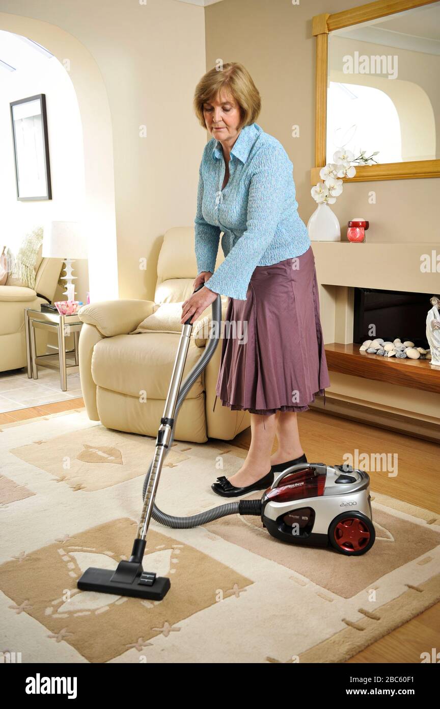 Donna anziana aspirapolvere nel suo salotto a casa. Una pulizia eccessiva può essere un segno di OCD, disturbo ossessivo Compulsivo. Foto Stock
