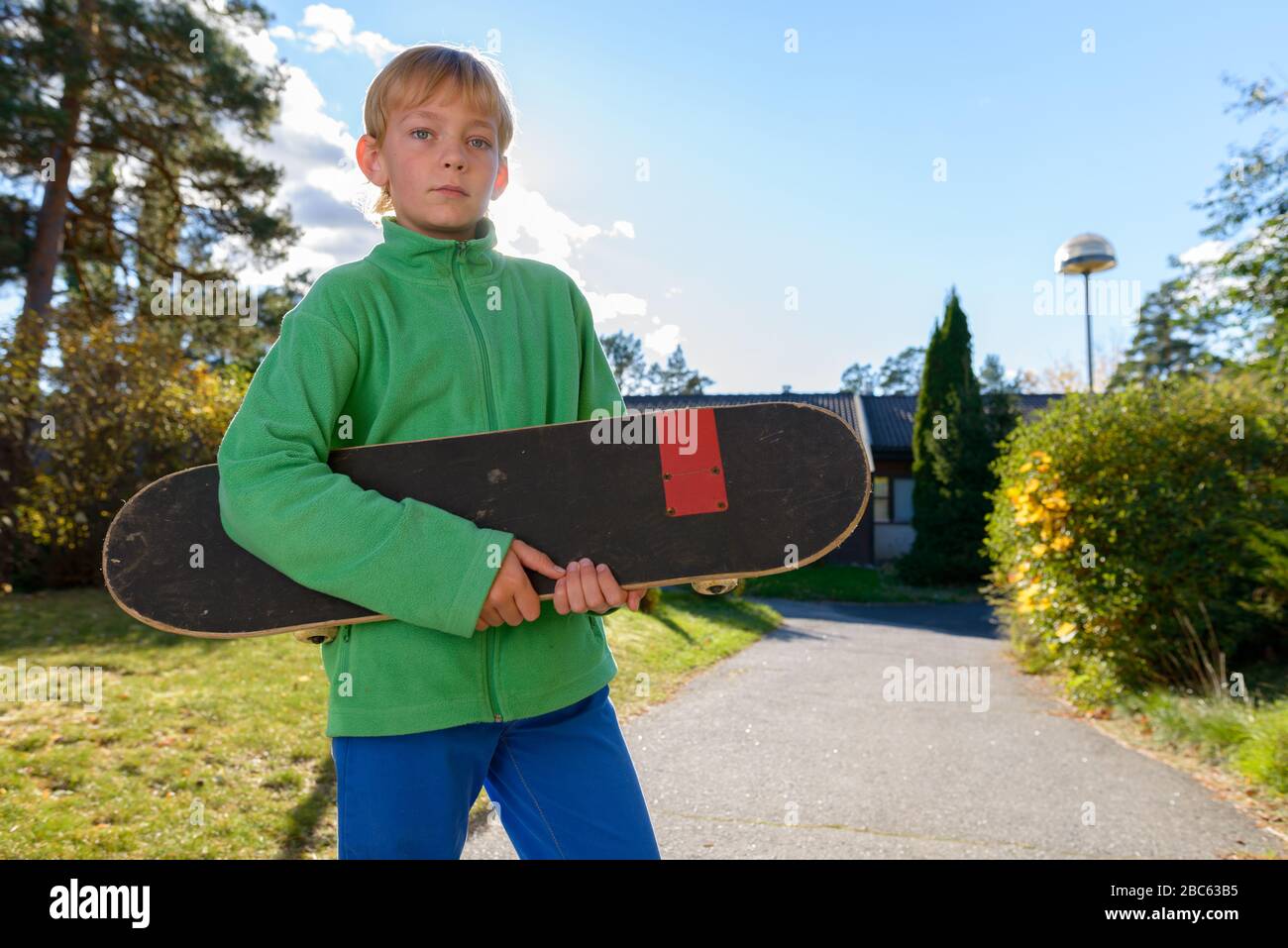 Giovane bel ragazzo che tiene skateboard nel cortile anteriore Foto Stock