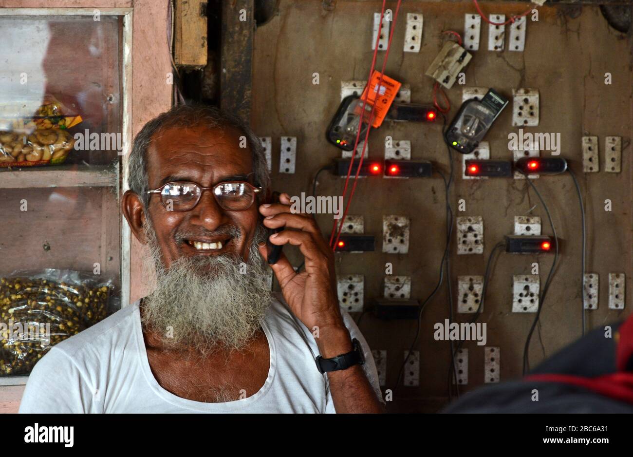 Un ottogenarian che fa la carica mobile messa a punto nel suo piccolo negozio al villaggio remoto dell'India la loro gente sta venendo per i telefoni cellulari che caricano. Foto Stock