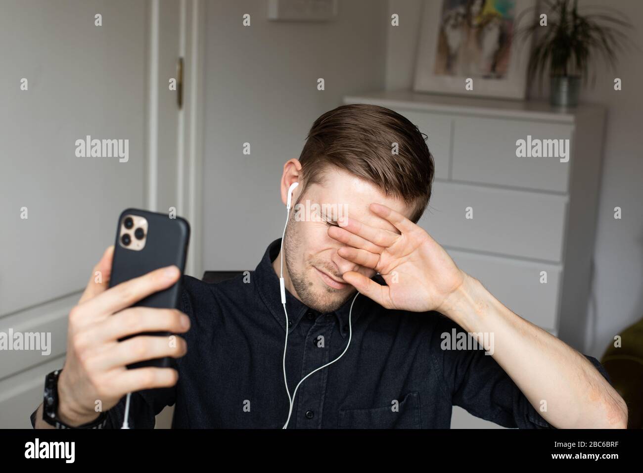 Uomo stanco e ansioso che ha una videochiamata in conferenza Zoom tramite smartphone. Ufficio domestico. Soggiorno a casa e lavoro da casa concetto durante Coronavirus Foto Stock