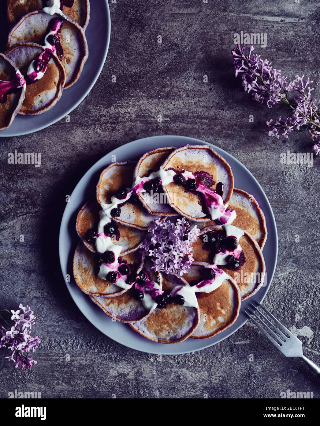 Frittelle viola con mirtilli e crema decorata con fiori lilla su sfondo scuro in primavera Foto Stock