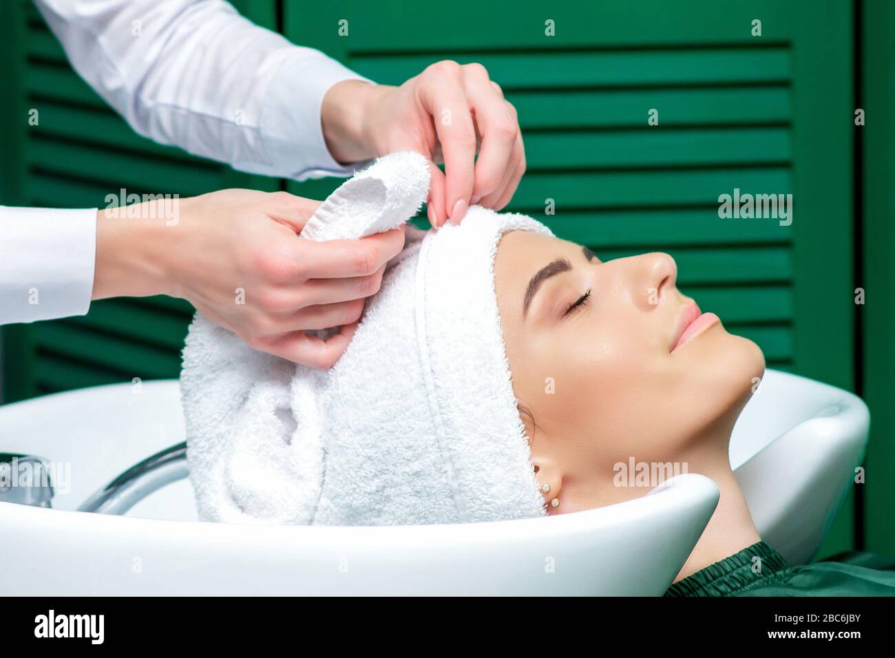 Parrucchiere che avvolge i capelli della donna in asciugamano dopo aver lavato la testa nel salone di bellezza, primo piano. Foto Stock