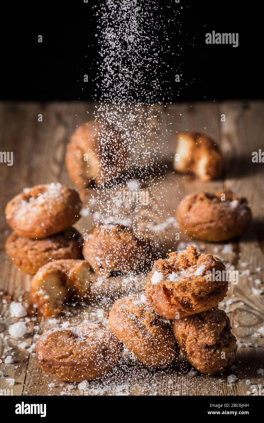 Uno zucchero spruzzato che cade su ciambelle fritte che si trovano sopra un asse di legno. Foto Stock