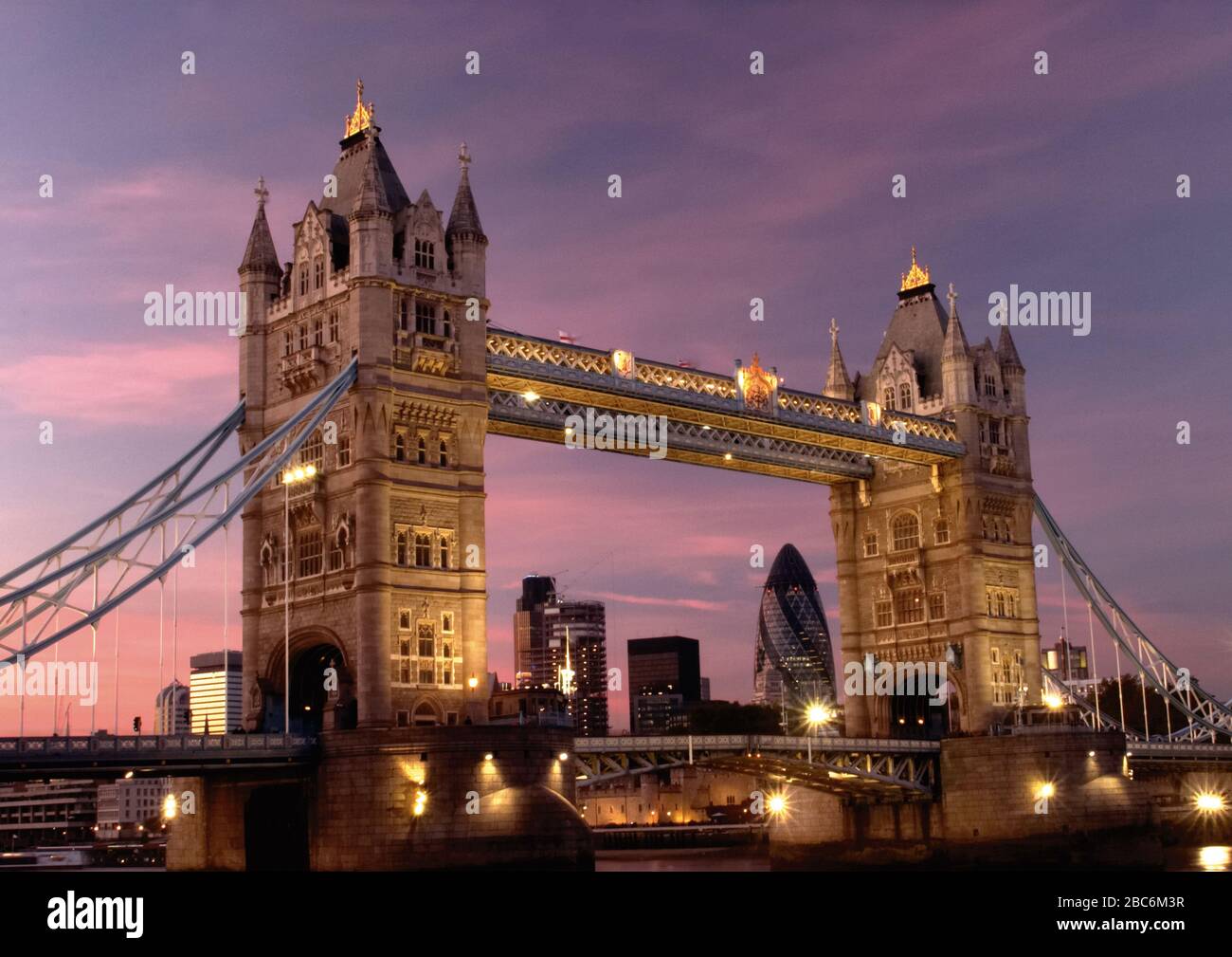 Guardando attraverso il Tower Bridge da Butler's Wharf sulla riva del Tamigi al Gherkin e ad altri grattacieli con un cielo rosa tramonto. Foto Stock