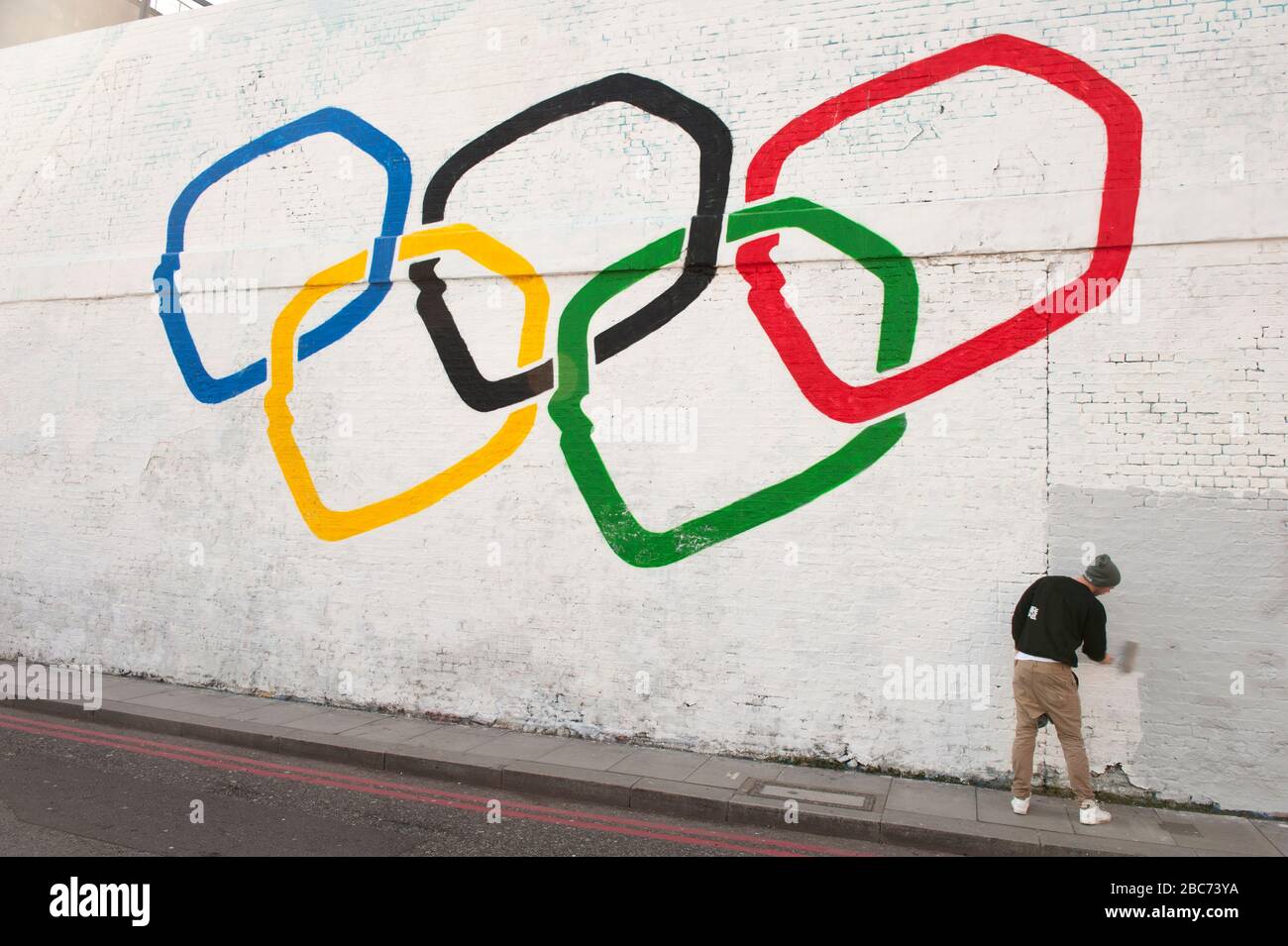 Un artista di strada dipinge anelli olimpici su un muro a Shoreditch, Londra, Regno Unito Foto Stock
