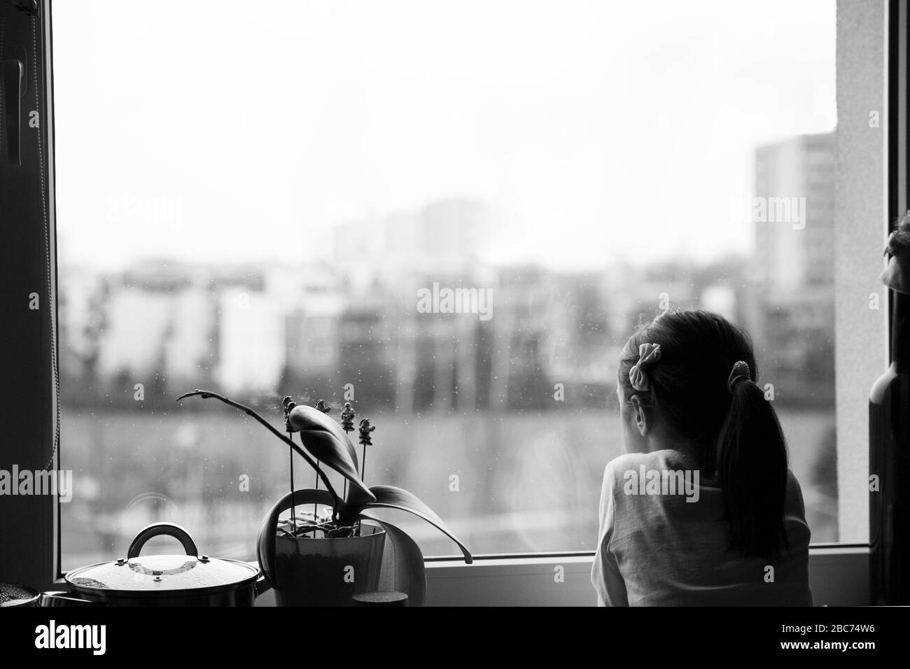 Giovane ragazza che guarda fuori attraverso la finestra, non in grado di andare fuori. Foto Stock