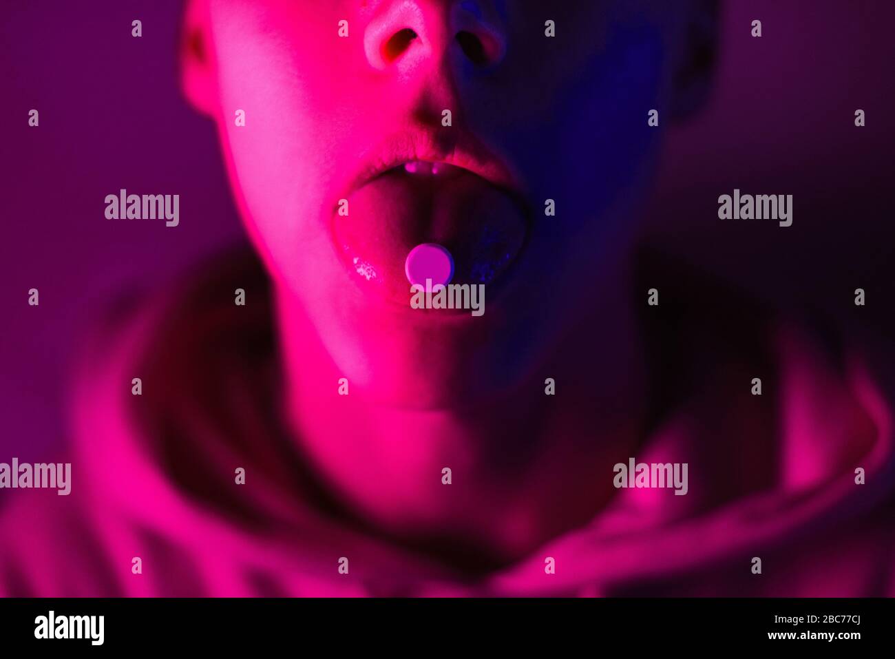 Giovane adolescente in una felpa con cappuccio rosa prende una droga in pillole. Tipo di timone con ruota lsd. Foto Stock