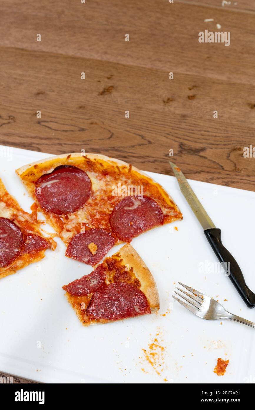 Una pizza al salame si trova affettata durante un pasto su un tagliere bianco. Foto Stock