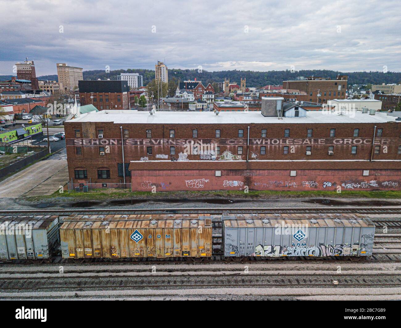 Un'occhialata dietro i binari della ferrovia e un edificio storico nel centro di Huntington con una vista del centro città sullo sfondo. Foto Stock