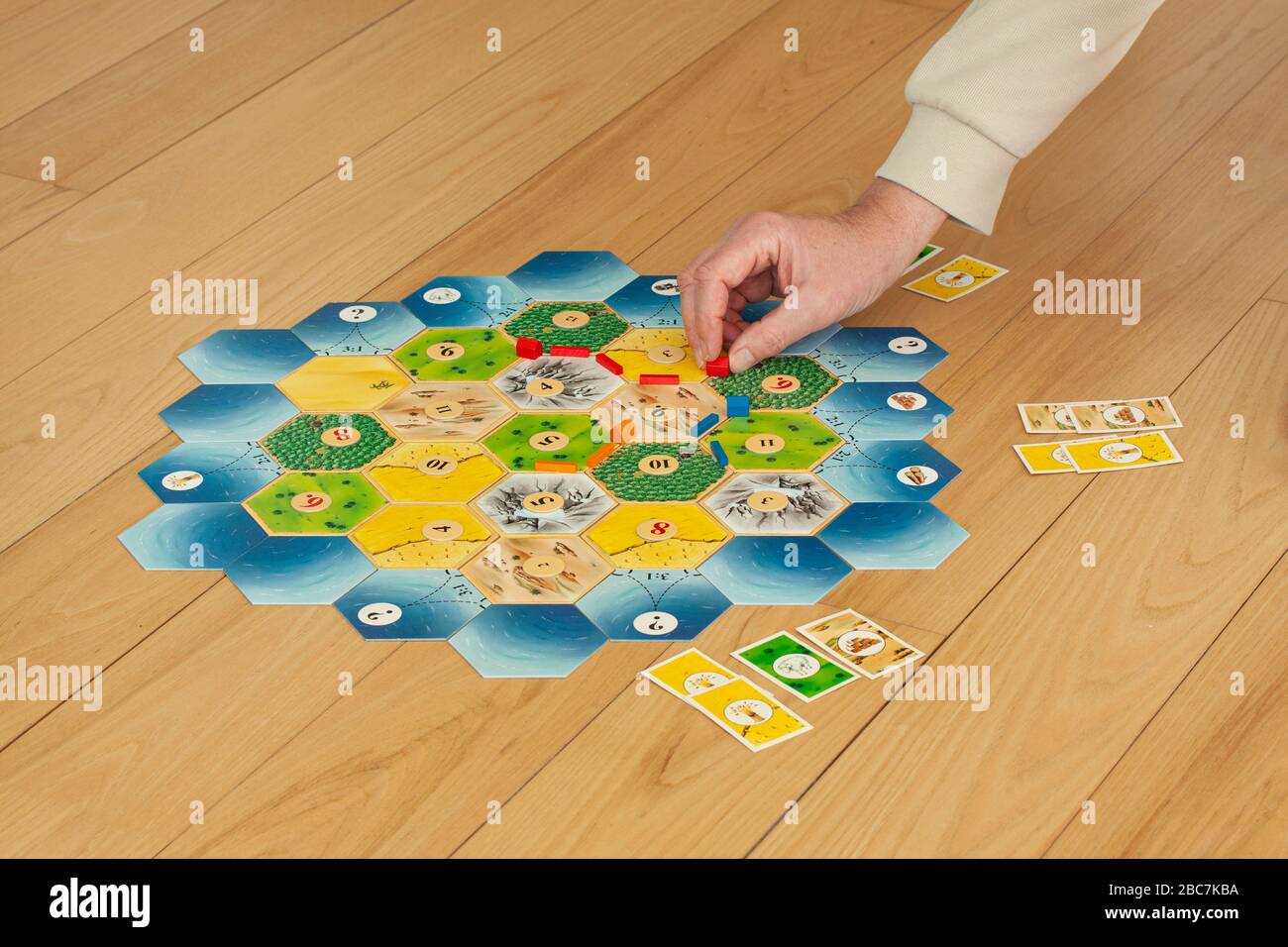 Vista dall'alto dei Settlers un popolare gioco da tavolo strategico di Catan su un tavolo di legno. Una mano sta tenendo una casa rossa. Copenaghen, Danimarca – 3 aprile 20 Foto Stock