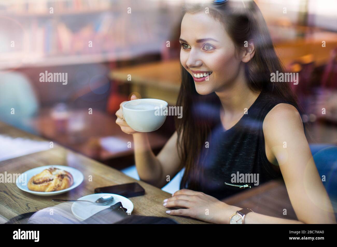 Giovane donna vista attraverso la finestra del caffè Foto Stock