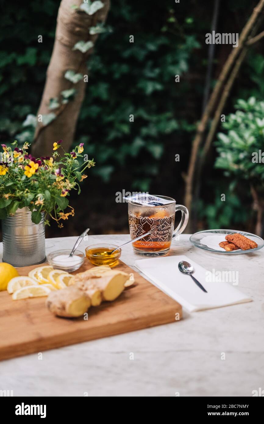 Tè in una tazza di vetro con limone, zenzero, miele, zucchero su tavola di legno in giardino. Fettine di limone e un cucchiaio con miele al tè caldo. Foto Stock