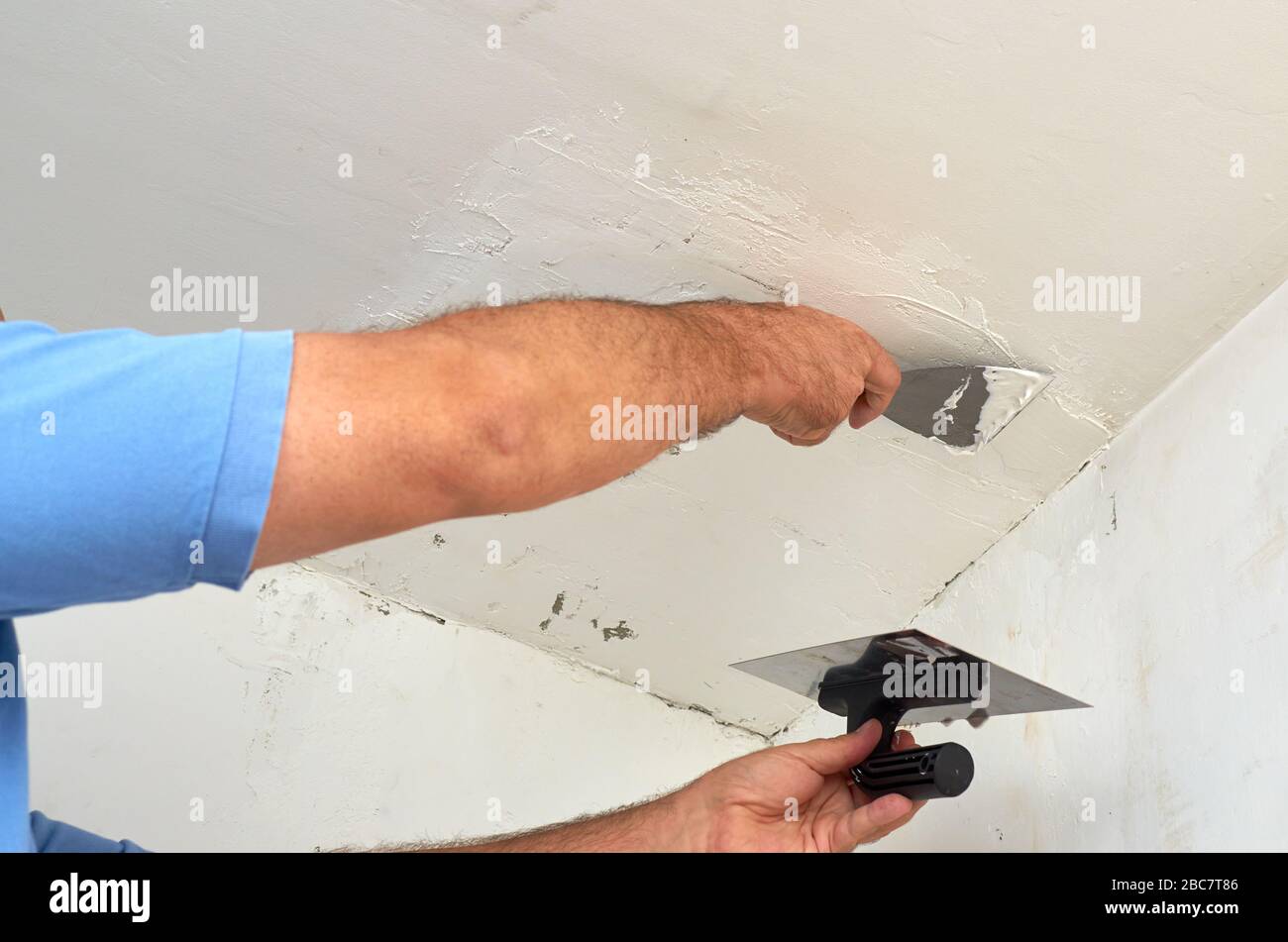 Uomo che mette lo spackle su un soffitto durante i lavori di ristrutturazione Foto Stock
