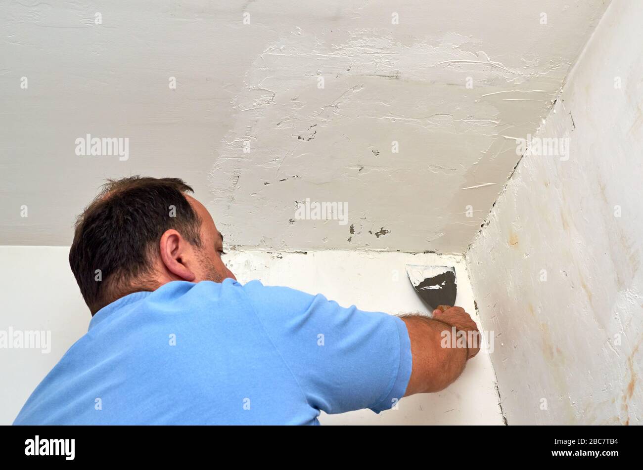 Uomo che mette lo spackle con una spatola su una parete durante i lavori di ristrutturazione Foto Stock