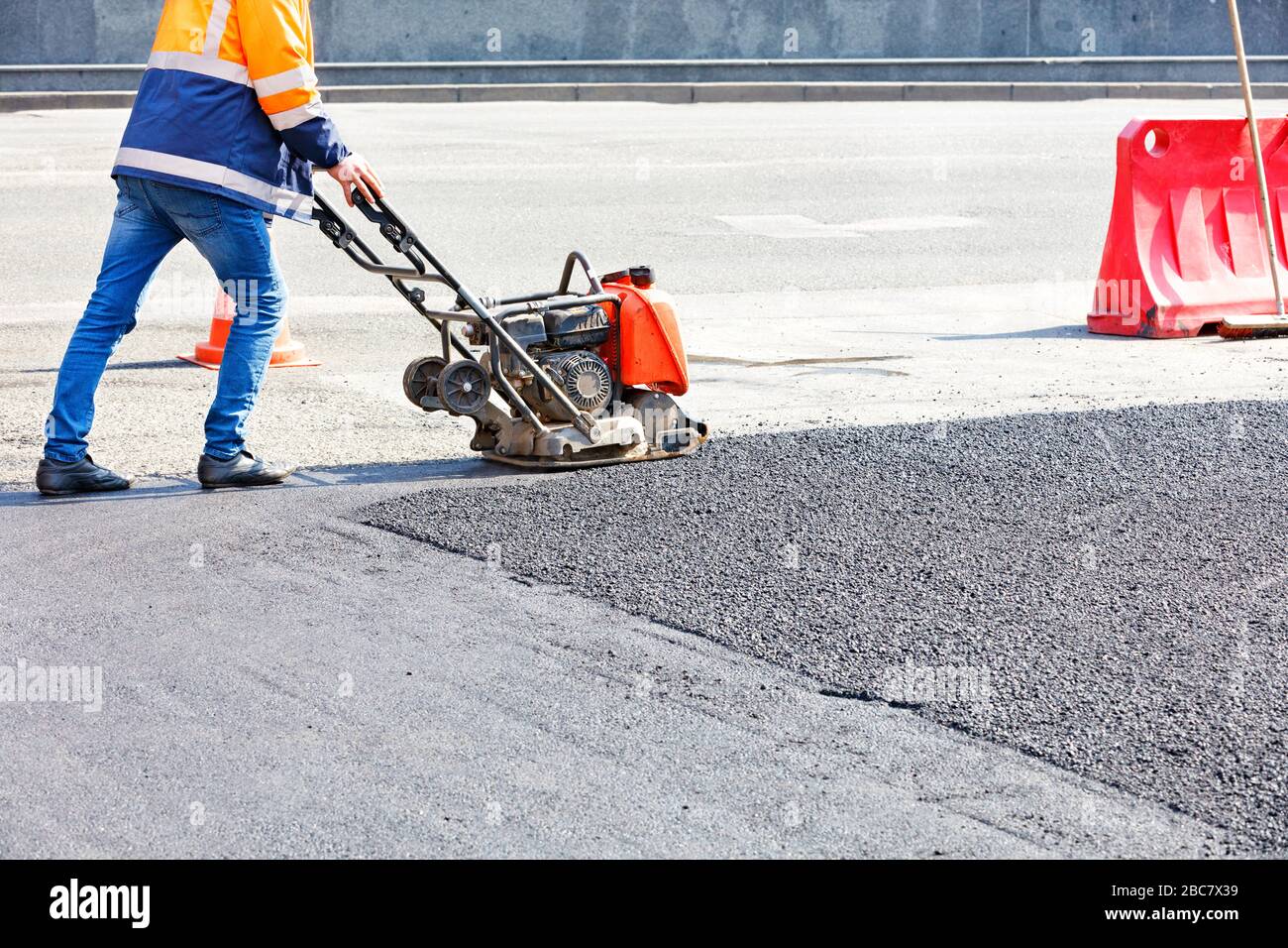 Gli addetti alla manutenzione su strada utilizzano compattatori a piastra vibrante che compattano l'asfalto nel sito di riparazione stradale. Foto Stock