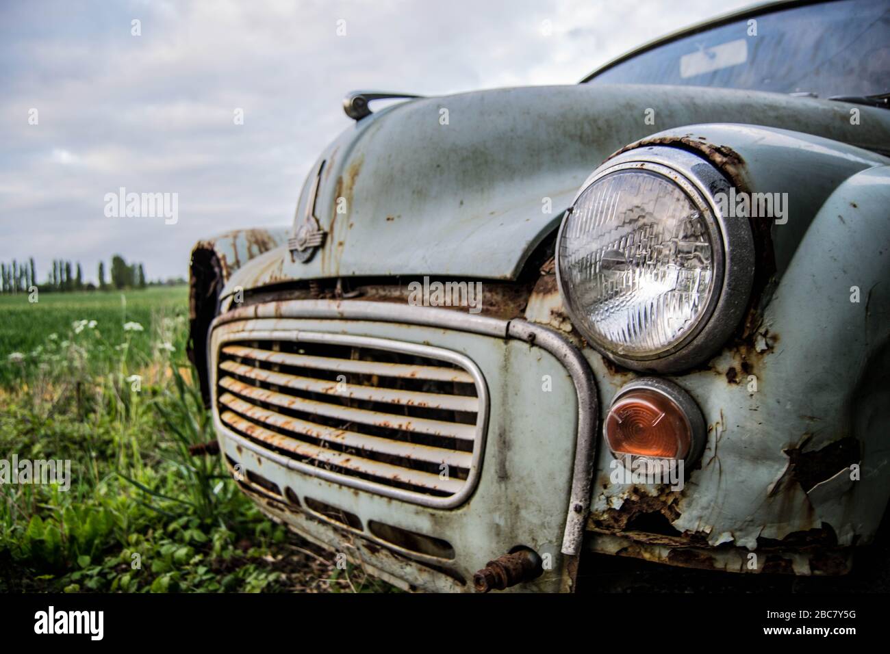 Un primo piano della parte anteriore di una vecchia auto arrugginita con un faro mancante Foto Stock