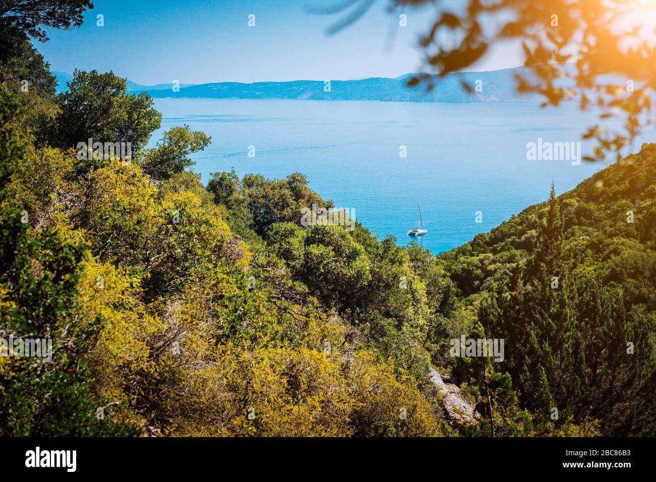 Vista panoramica ultra ampia dell'idilliaca cittadina a valle con tetti rossi sull'isola mediterranea. Oliveti, cipressi e baia blu in lontananza. Foto Stock