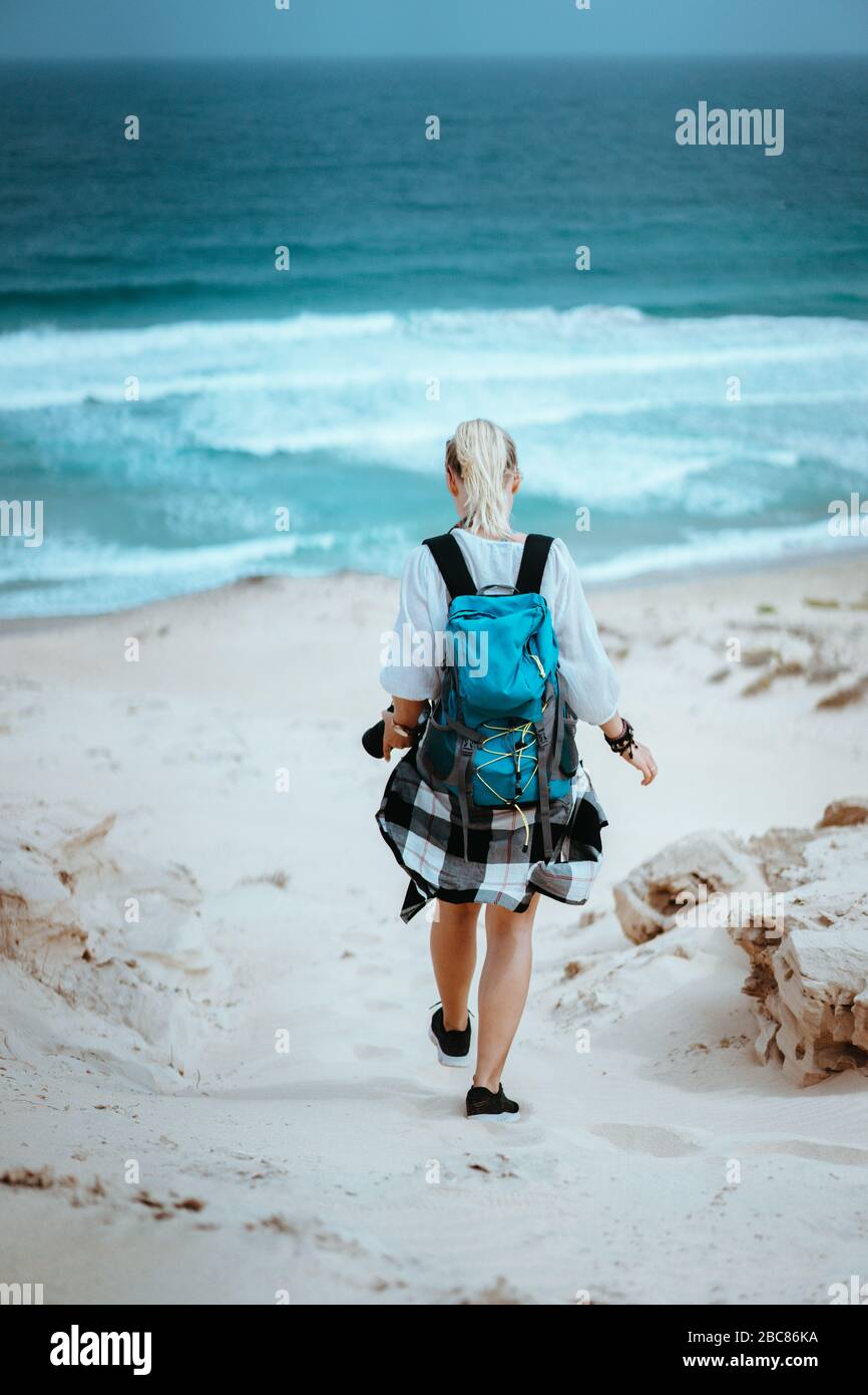 Donna escursionista con zaino scendendo una duna di sabbia verso la spiaggia solitaria. Sao Vicente Capo Verde. Foto Stock