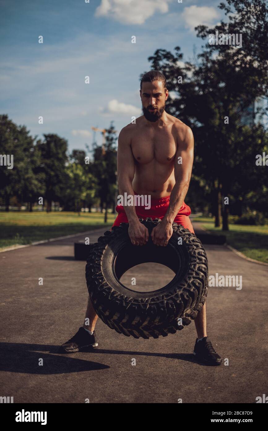 L'atleta di hipster solleva il pneumatico nel parco in una giornata di sole Foto Stock