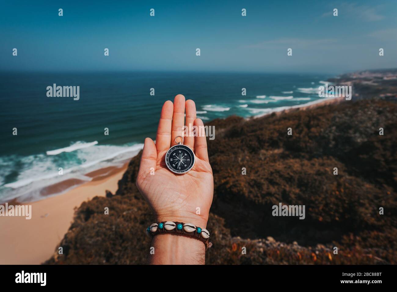 POV man mano con bussola. Avventura Symbolling-cerca di concetto contro il mare e le onde nel litorale in background. Foto Stock