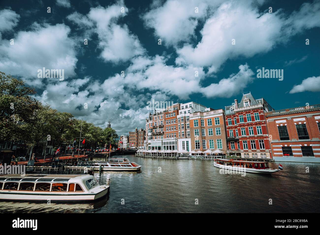 Classico paesaggio urbano di Amsterdam. Barche di crociera galleggiante sul canale, il river side promenade, caffetterie, tipica architettura olandese. Scena urbana e white fl Foto Stock