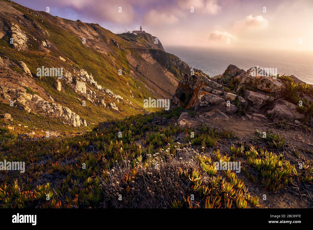 Faro di Cabo da Roca alla luce del sole e splendido paesaggio collinare della costa. Il punto più occidentale dell'Europa continentale, Sintra, Portogallo. Foto Stock