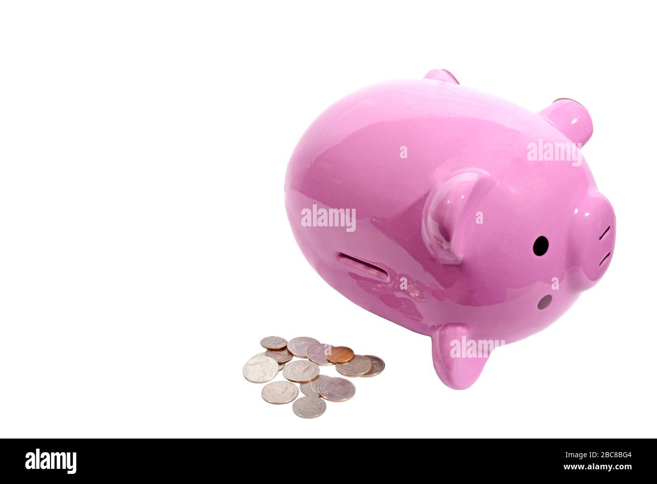 Scatto orizzontale di una banca piggy rosa che giace sul suo lato con la scanalatura sulla parte superiore rivolta verso la macchina fotografica. Pile di monete accanto ad esso. Sfondo bianco. C Foto Stock