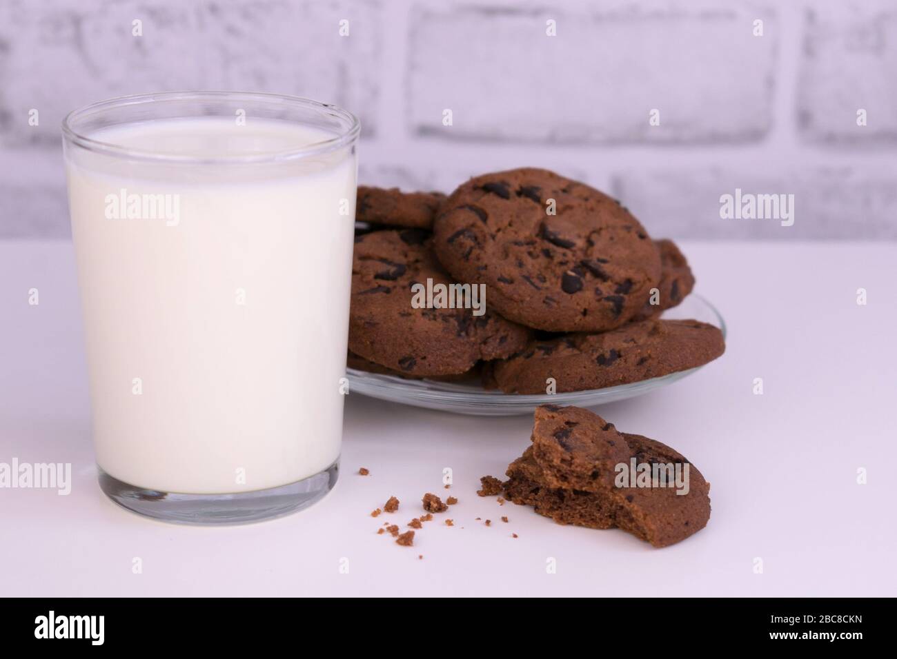 Bicchiere di latte e biscotti al cioccolato su sfondo bianco. Foto Stock
