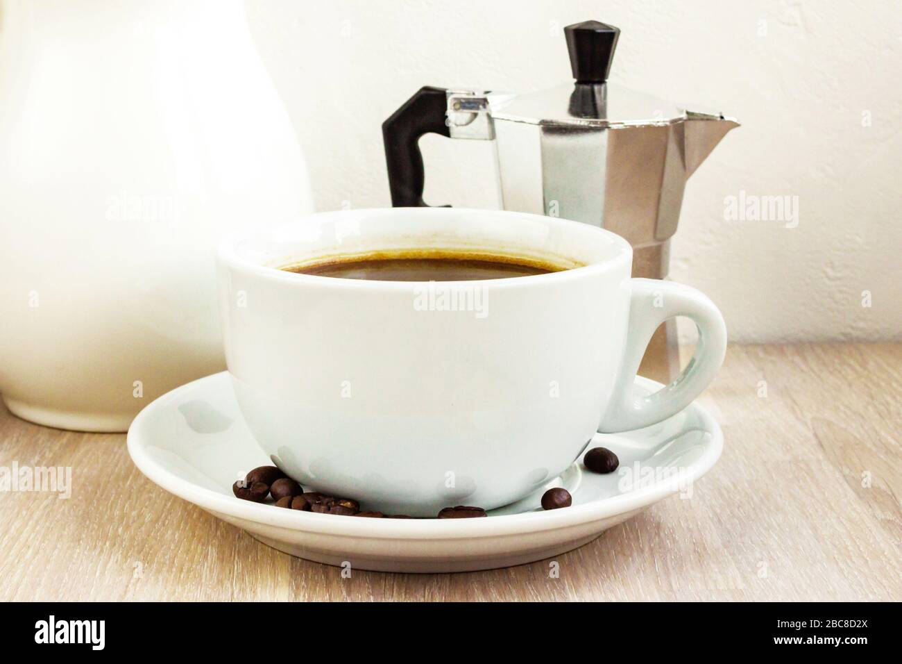 Tazza da caffè bianca, piattino e chicchi, macchina da caffè in alluminio, jag. Concetto di colazione Foto Stock